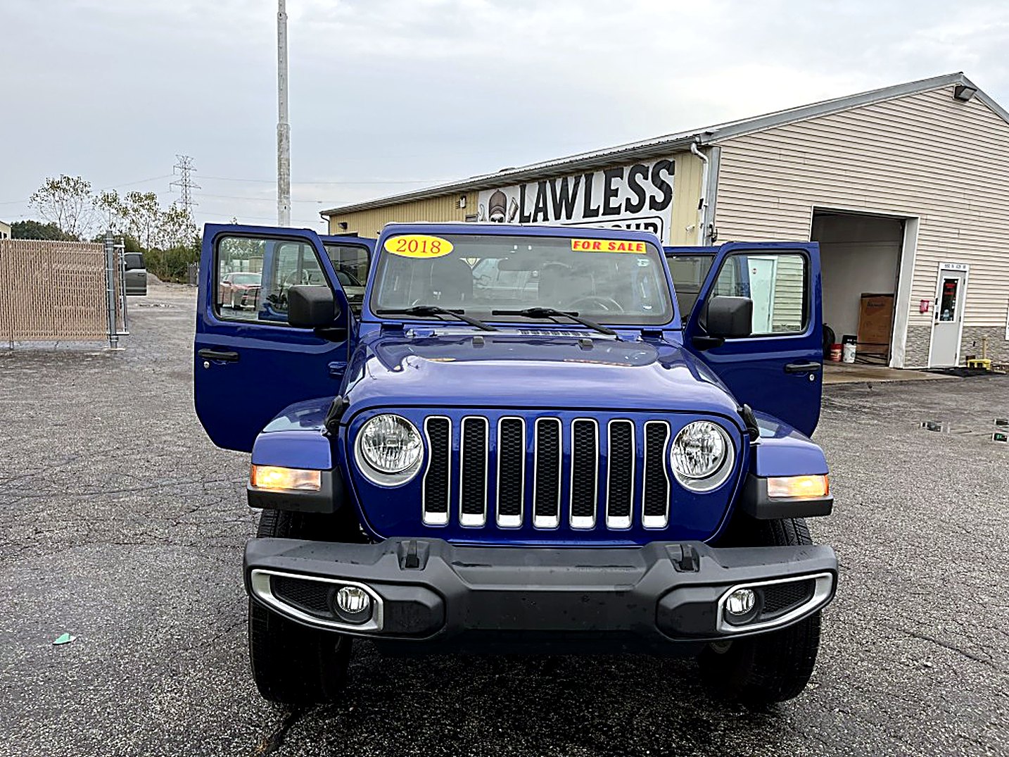 A blue Jeep Wrangler for sale in front of the Lawless Auto Group building
