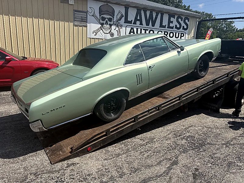 Green Pontiac LeMans on a flatbed in front of the Lawless Auto Group sign